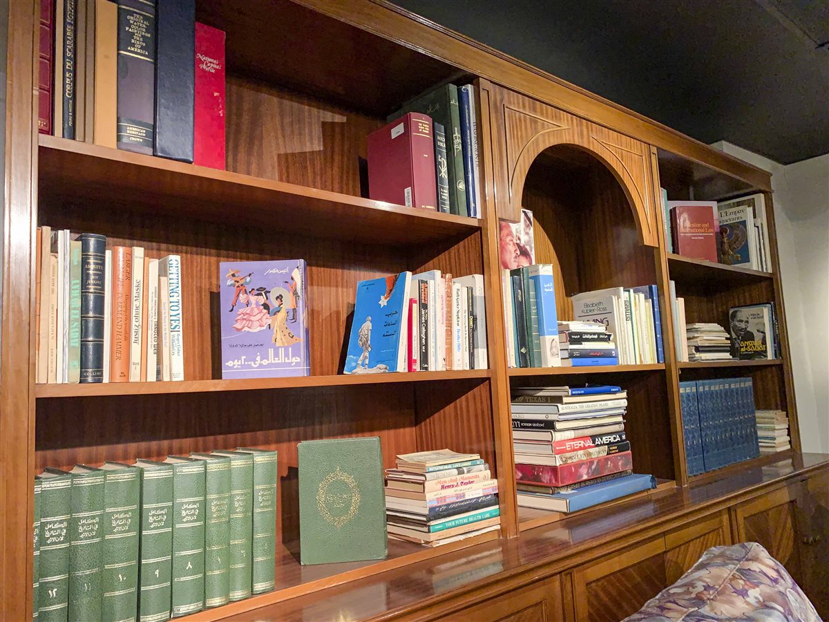 مكتبة خشبية دافئة اللون تحتضن كتبًا عربية وأجنبية