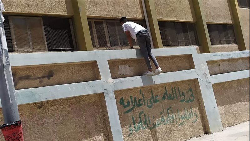 شخص يعتلي سور مدرسه